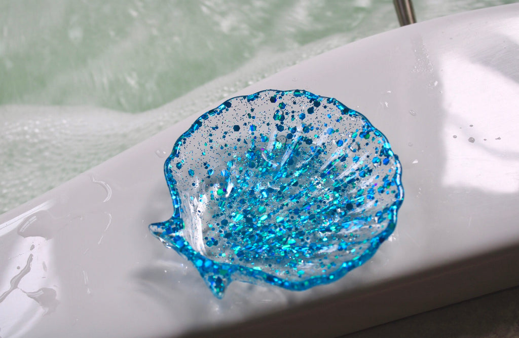 Blue glittery shell-shaped soap dish on a white surface with a blurred background