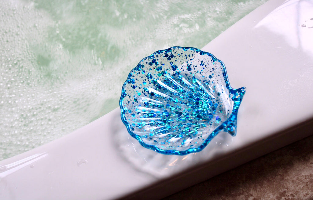 Blue glittery shell-shaped dish on a white surface with water in the background