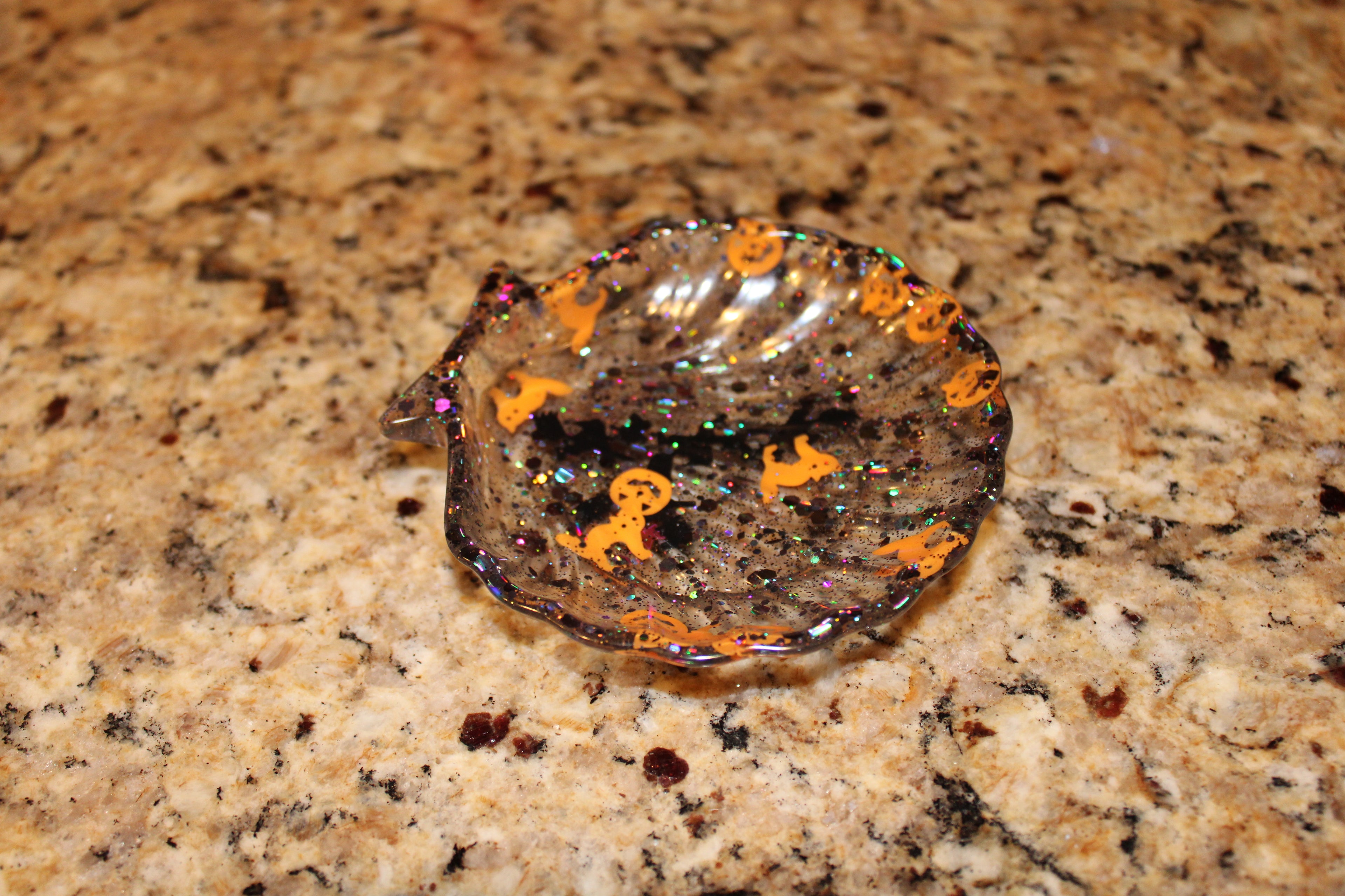 Resin artist crafts a sparkly, seashell-shaped Halloween candy dish with pumpkin and ghost decorations.