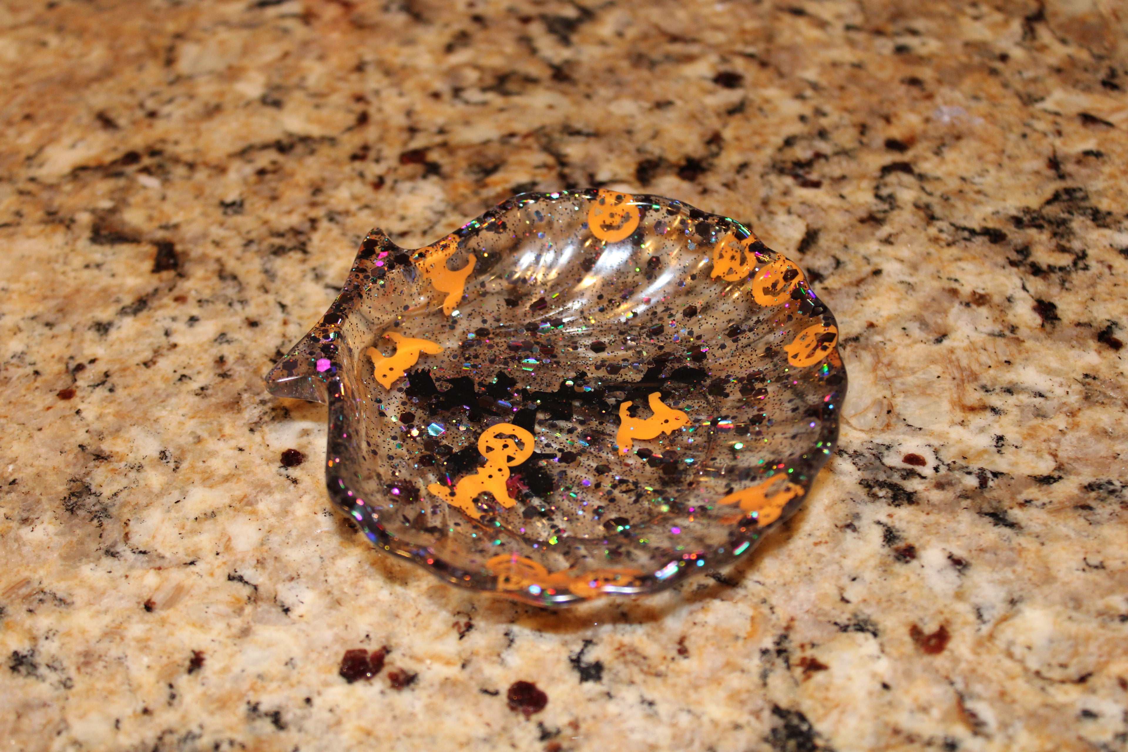 A festive, sparkly Halloween resin ashtray features ghosts and jack-o'-lanterns on a granite countertop.
