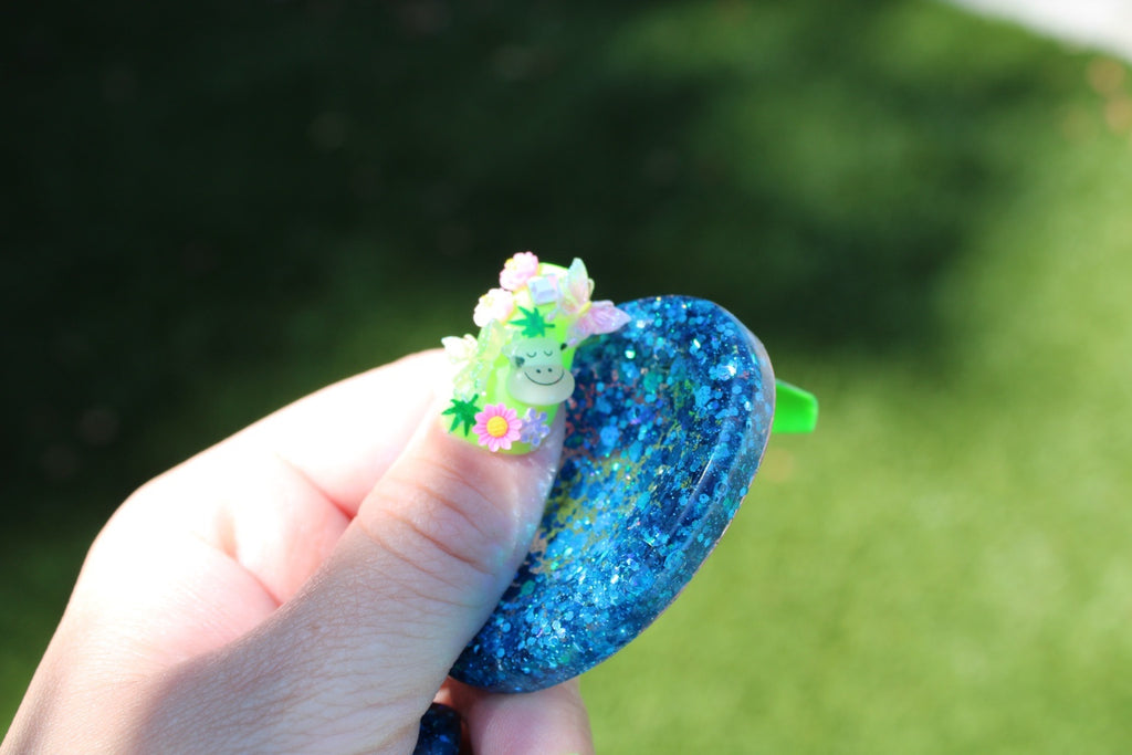 A hand holding a small, glittery blue oval anxiety token against a blurred green outdoor background.