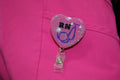 A registered nurse's (RN) pink scrubs display a glittery heart-shaped badge reel featuring "RN" and a stethoscope.