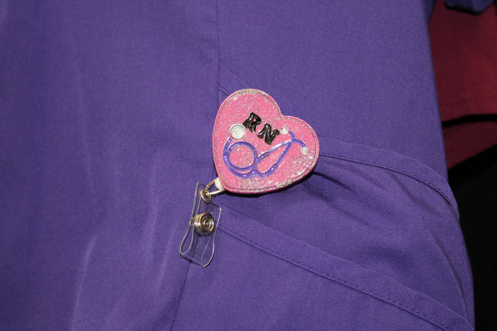 A nurse wears a purple uniform with a pink, glittery RN badge featuring a stethoscope.