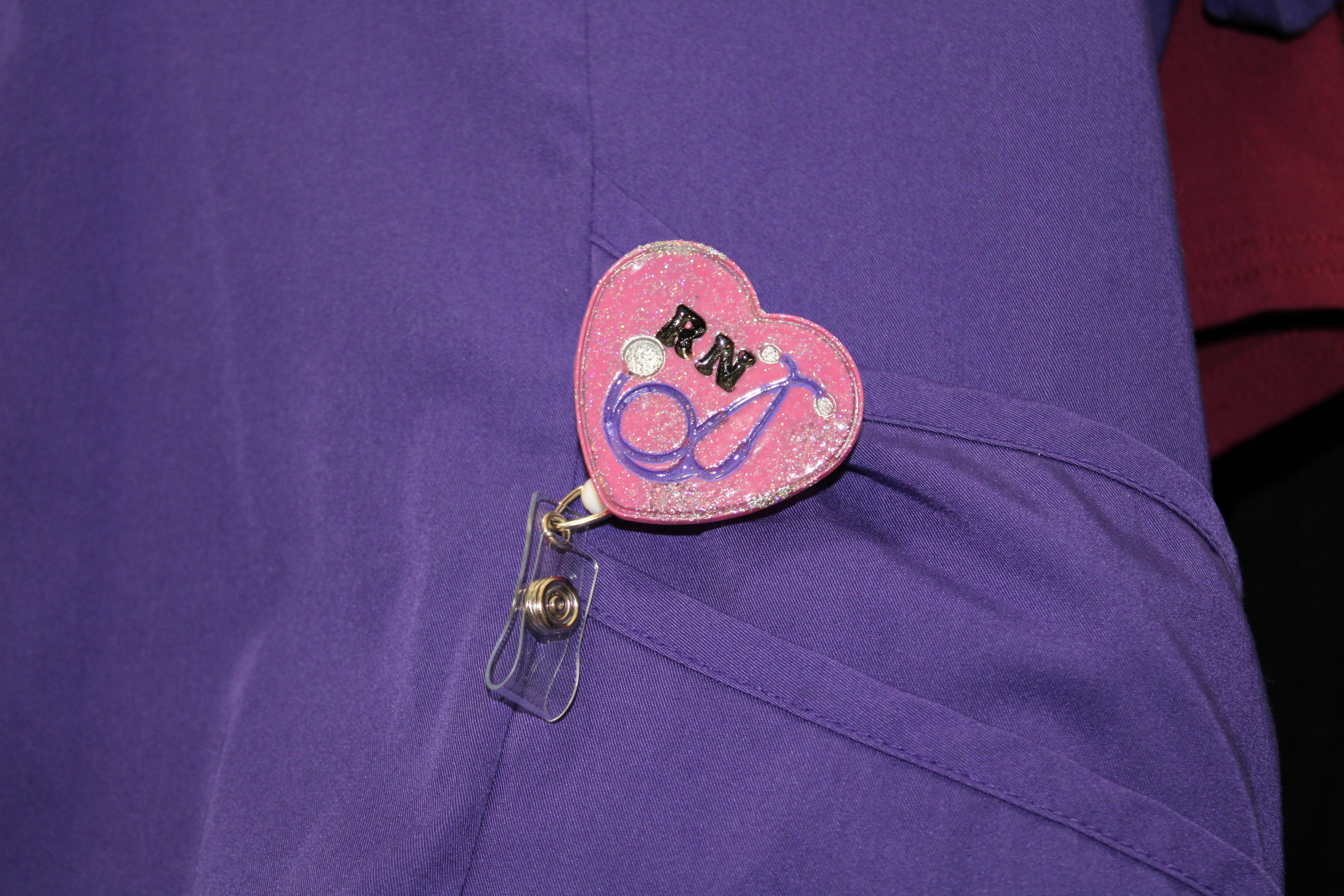 A nurse wears a purple uniform with a pink, glittery RN badge featuring a stethoscope.