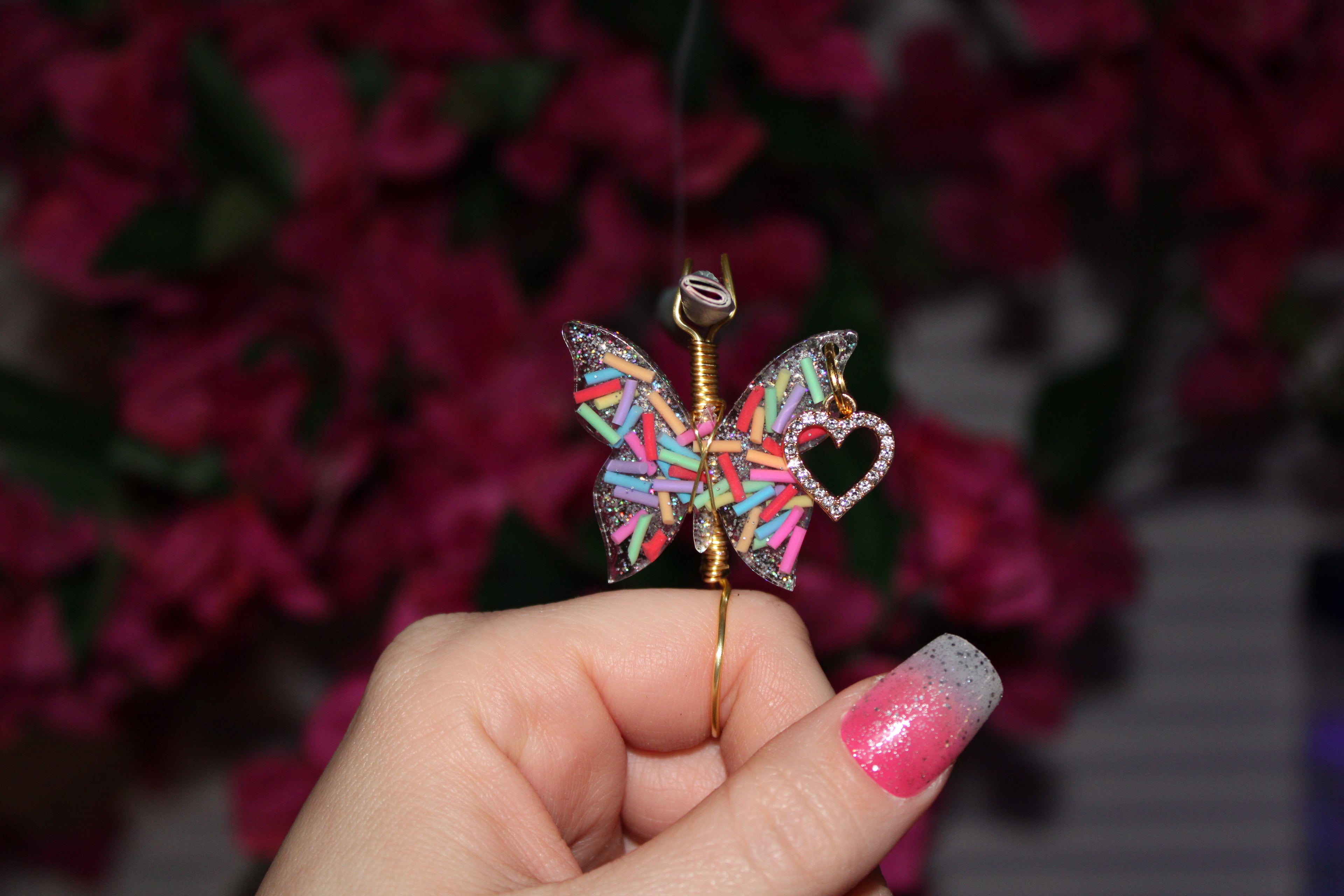 Colorful butterfly-shaped smoke ring held in a hand with a blurred floral background