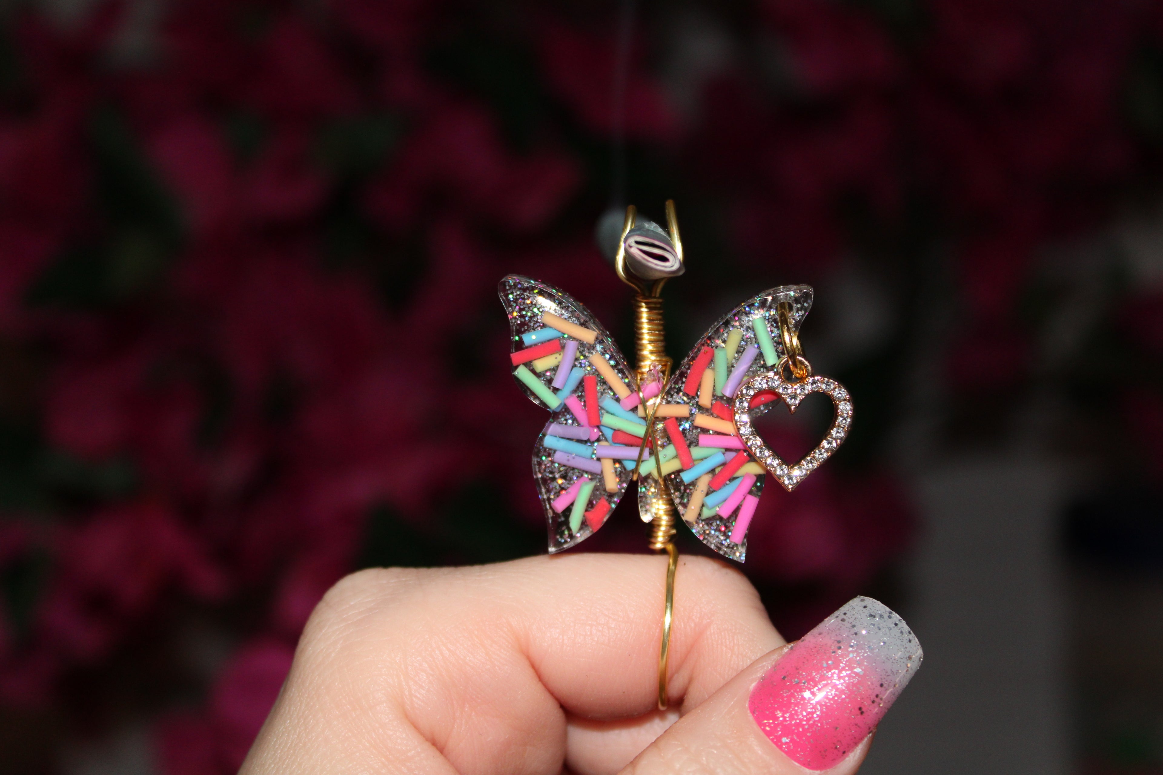 Butterfly-shaped smoke ring with colorful sprinkles held by a hand against a dark background