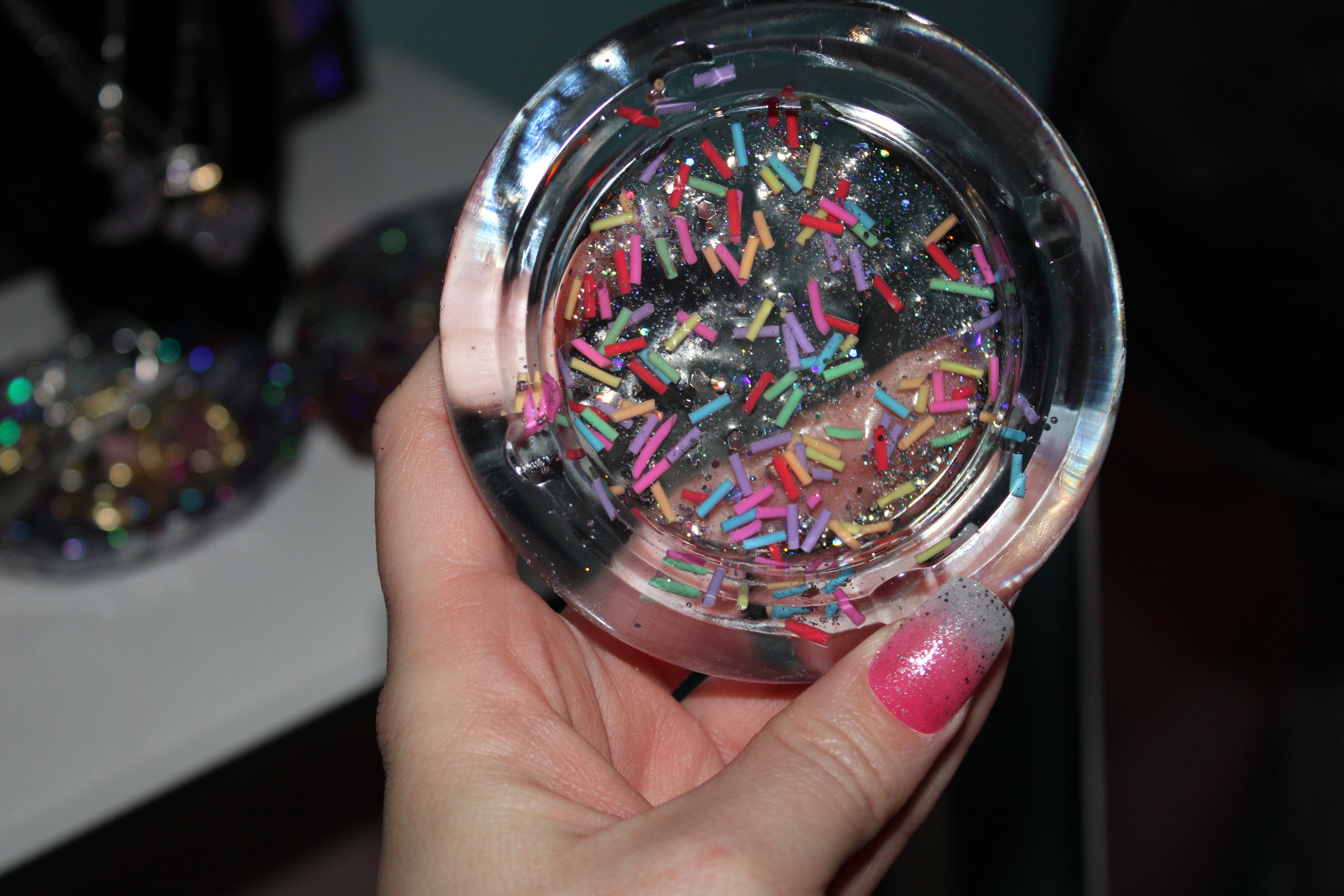 Hand holding a round, transparent ashtray filled with colorful sprinkles.