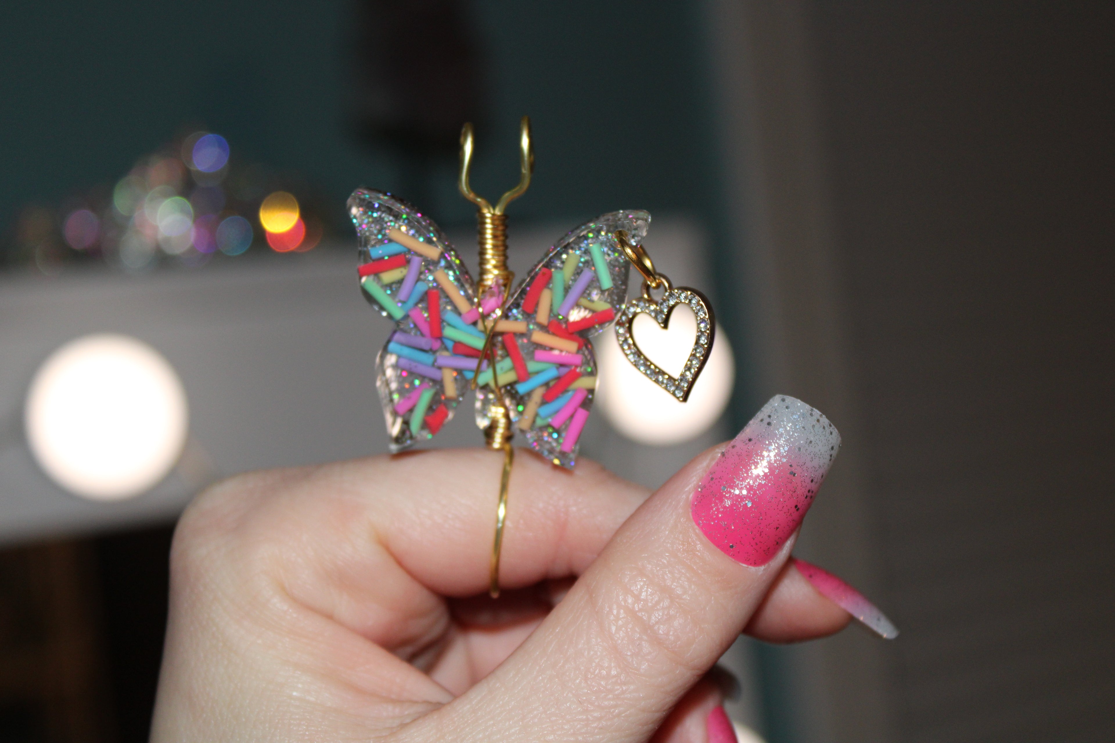 Butterfly-shaped smoke ring with colorful sprinkles and a heart charm held by a hand.