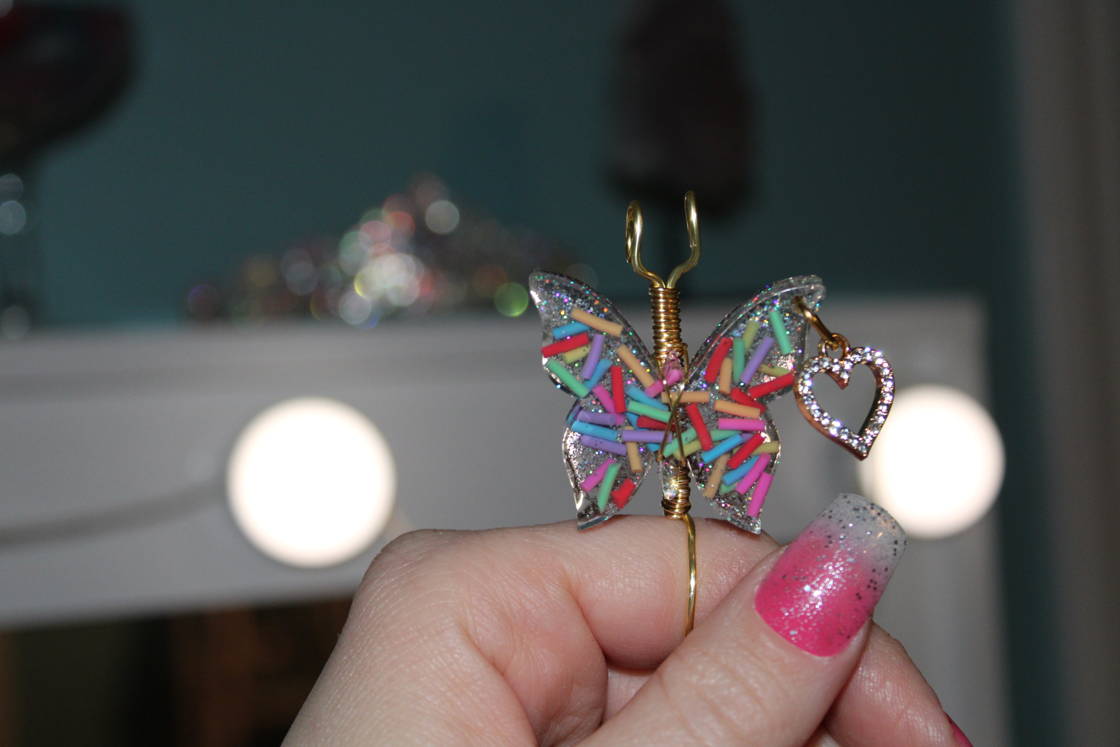 Colorful butterfly-shaped smoke ring held by a hand with pink nail polish.