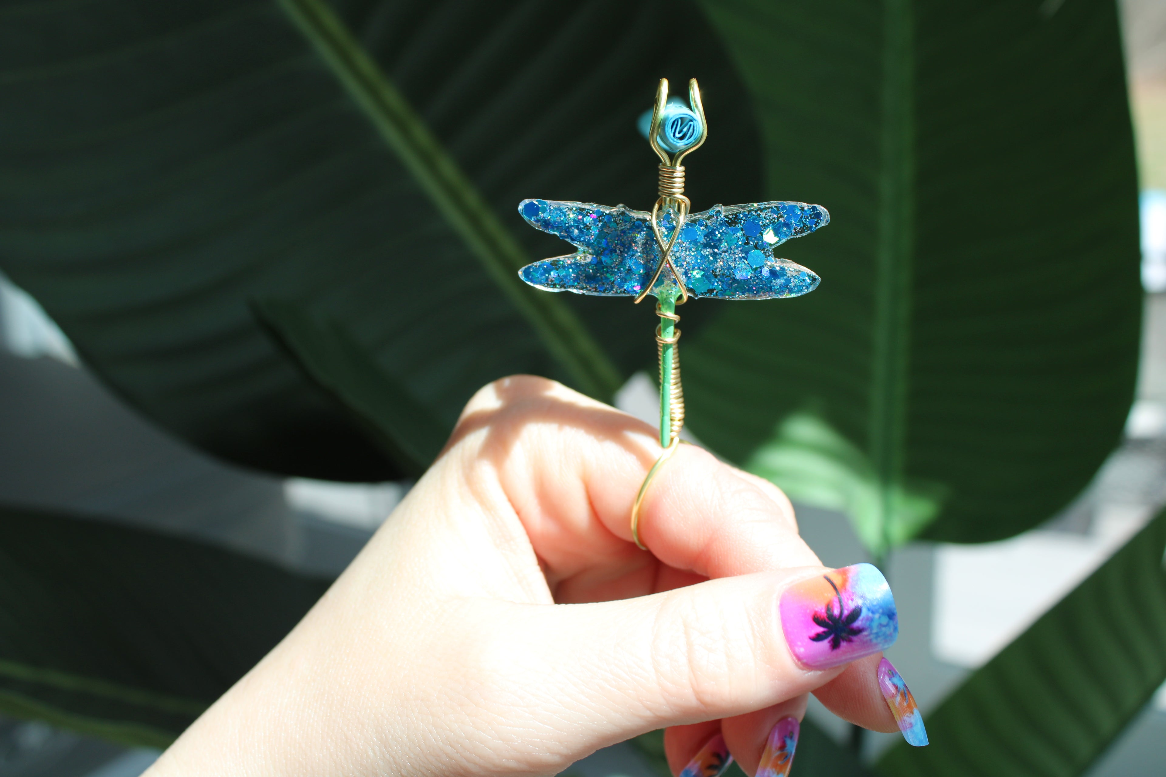 Hand holding a decorative dragonfly smoke ring with a blurred green leaf background
