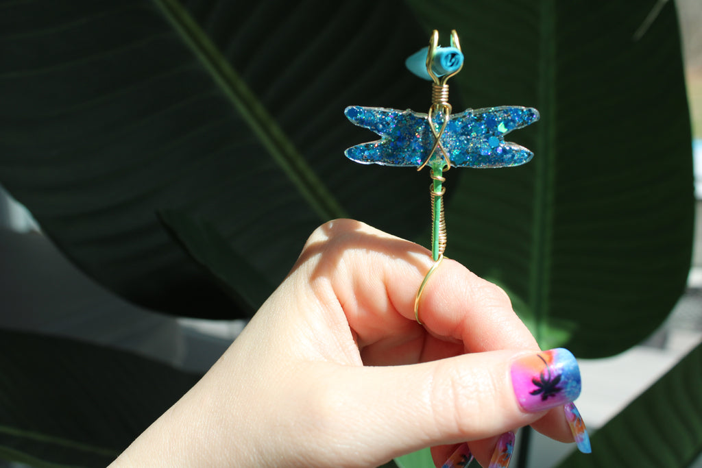 Hand holding a decorative dragonfly smoke ring against a leafy background