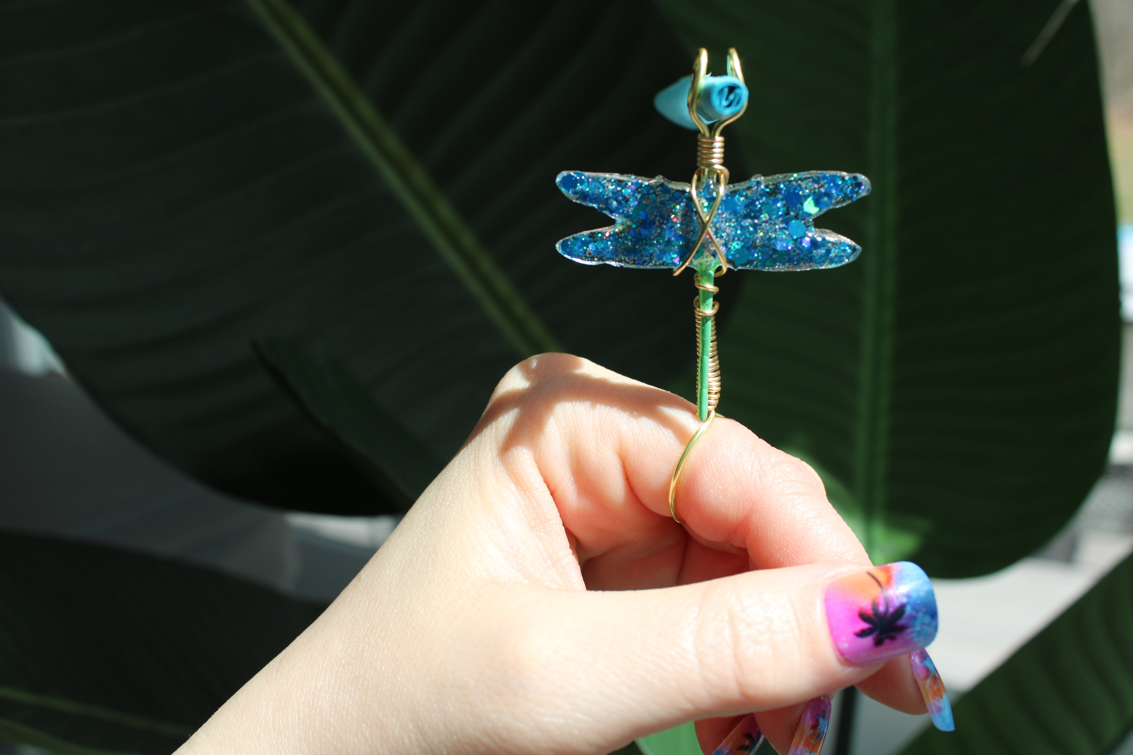 Hand holding a decorative dragonfly smoke ring against a leafy background