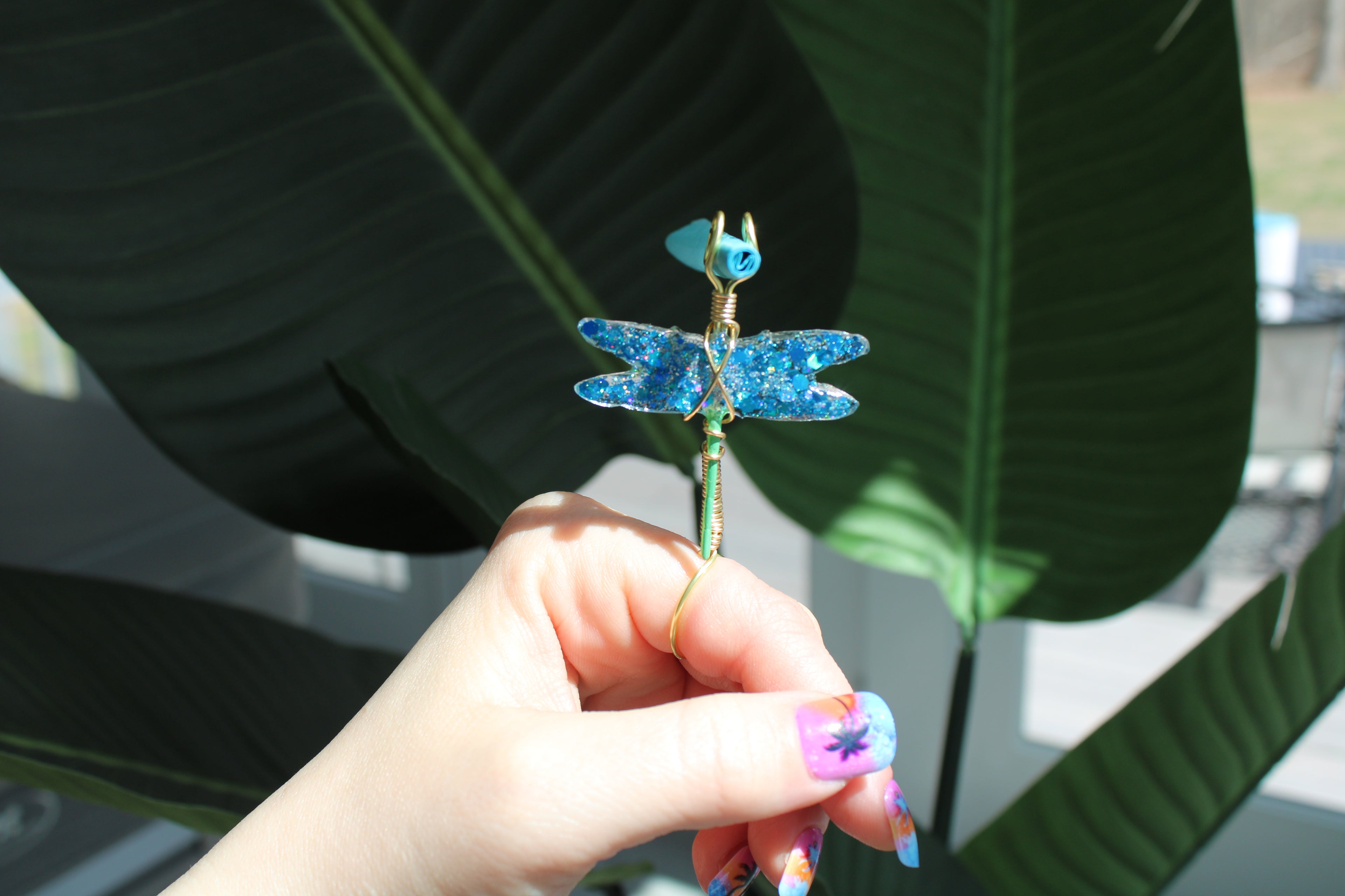 Hand holding a decorative dragonfly smoke ring against a leafy background
