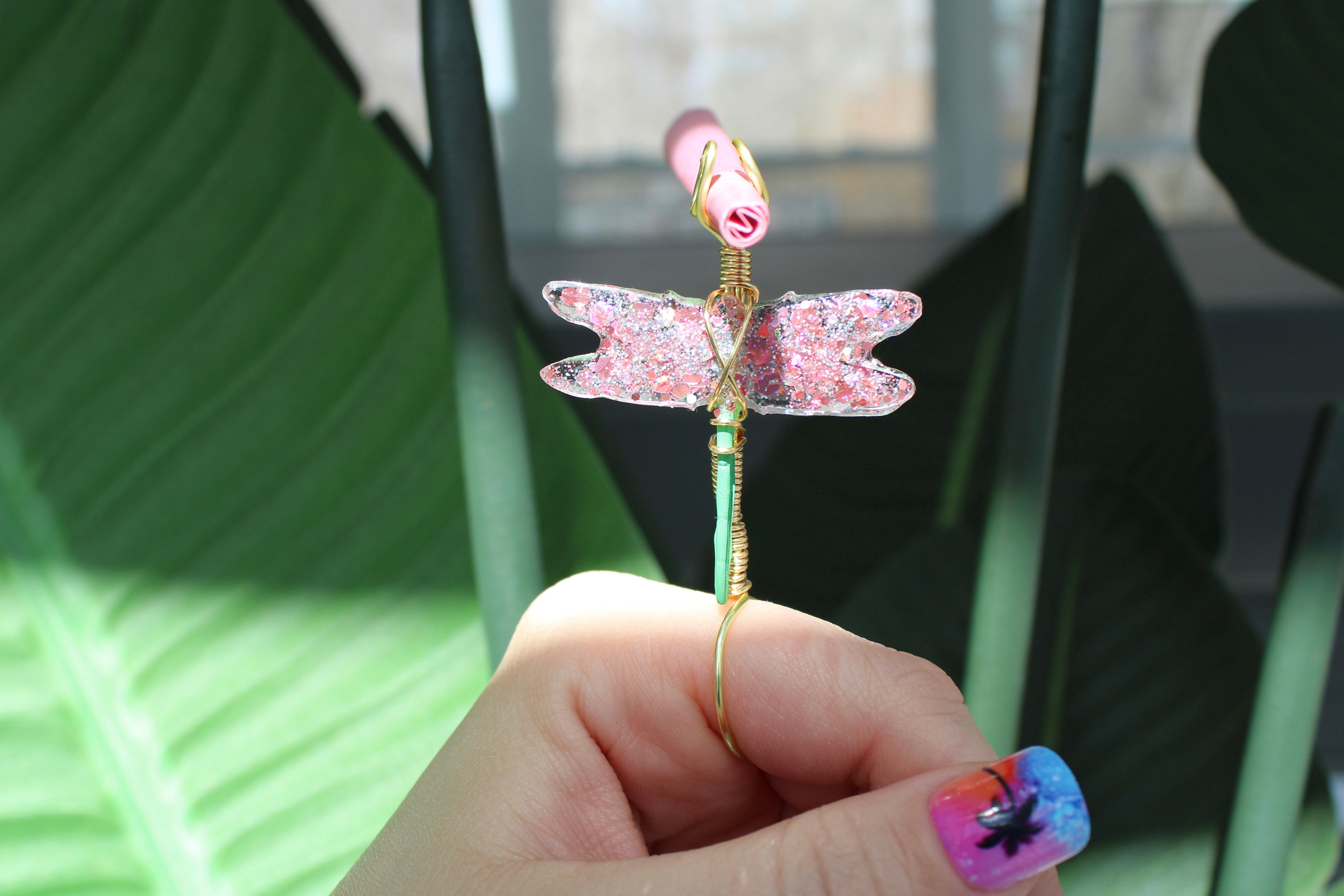 Hand holding a decorative dragonfly smoke ring with pink and gold details.
