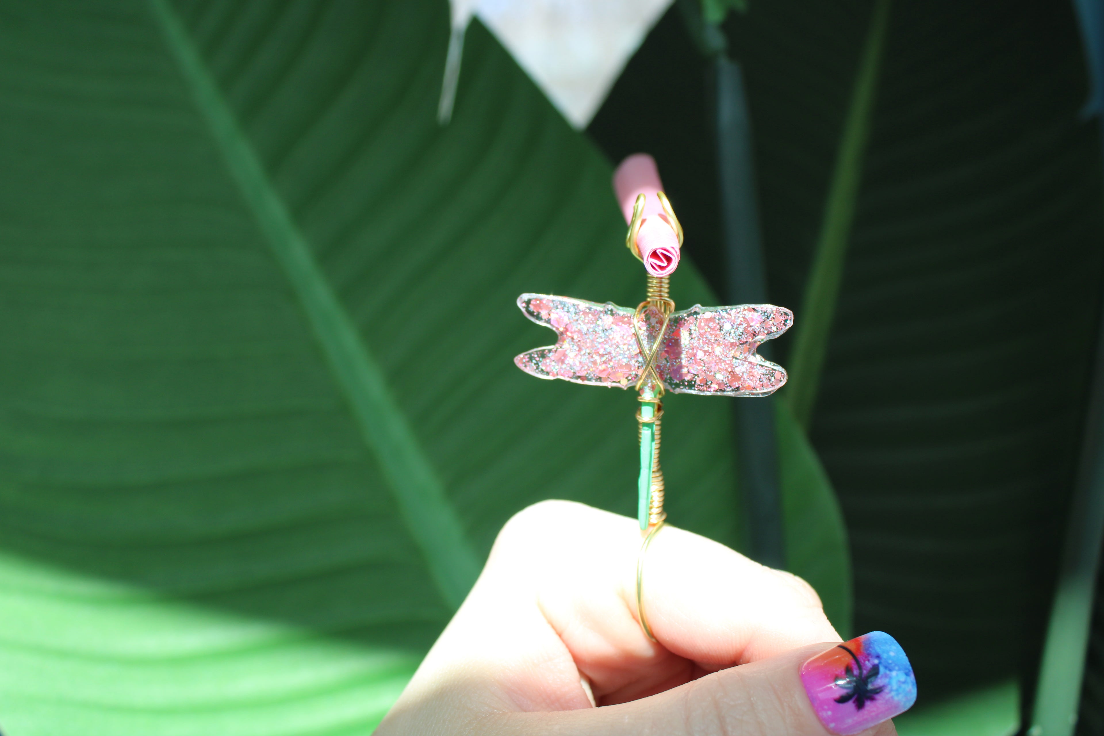 Hand holding a dragonfly smoke ring against a green leafy background