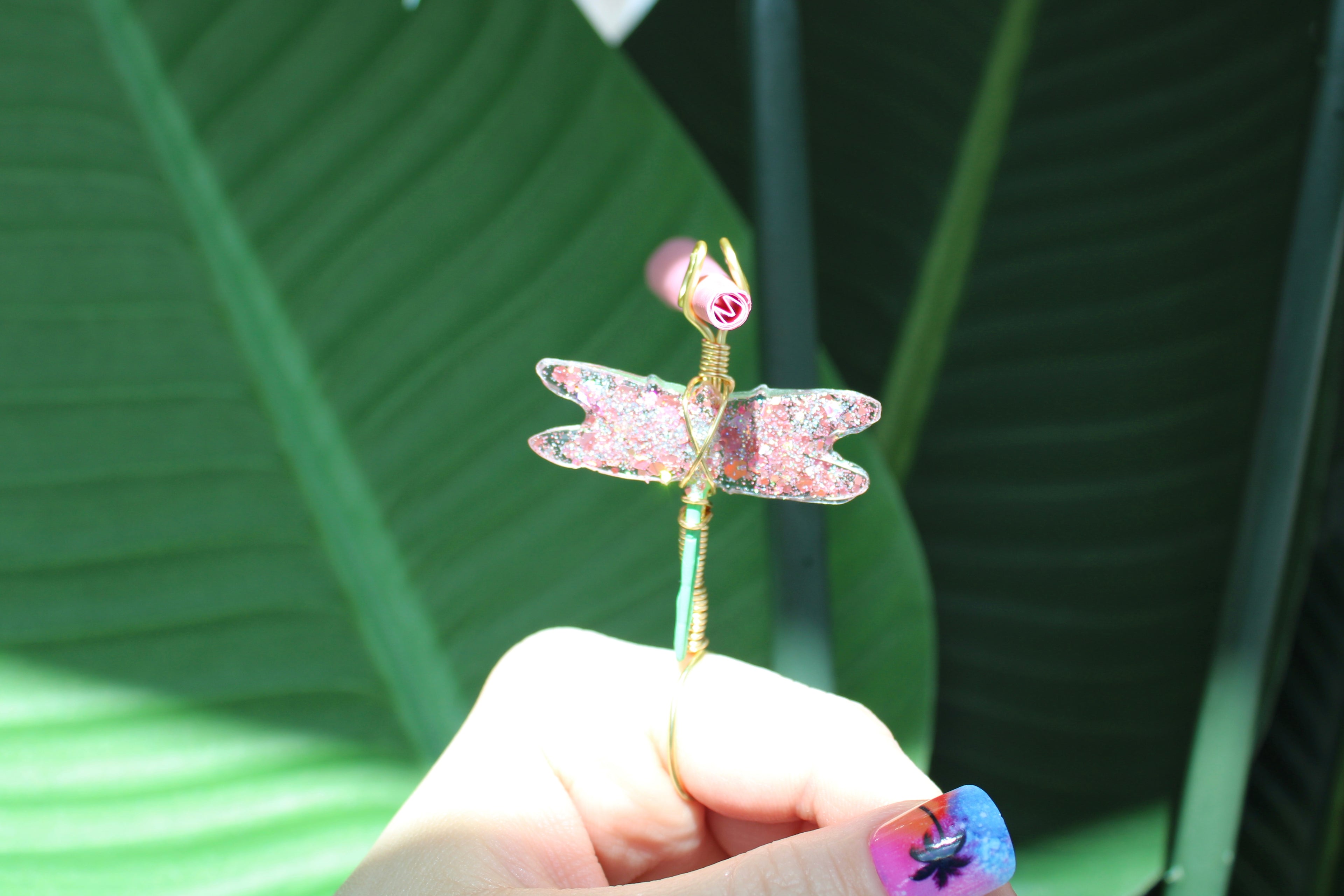 Hand holding a decorative dragonfly smoke ring against a green leafy background