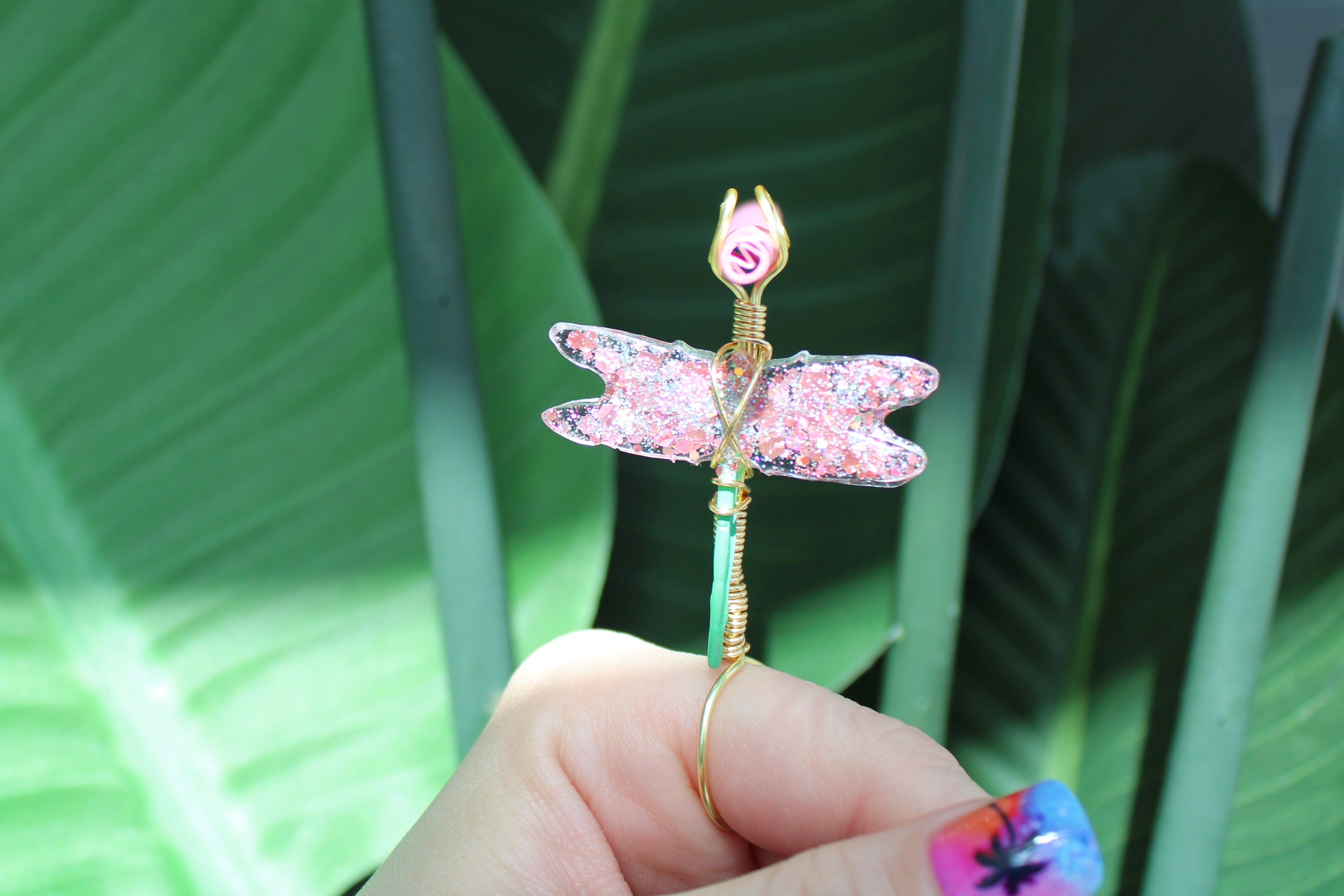 Hand holding a pink dragonfly-shaped smoke ring against a green leafy background