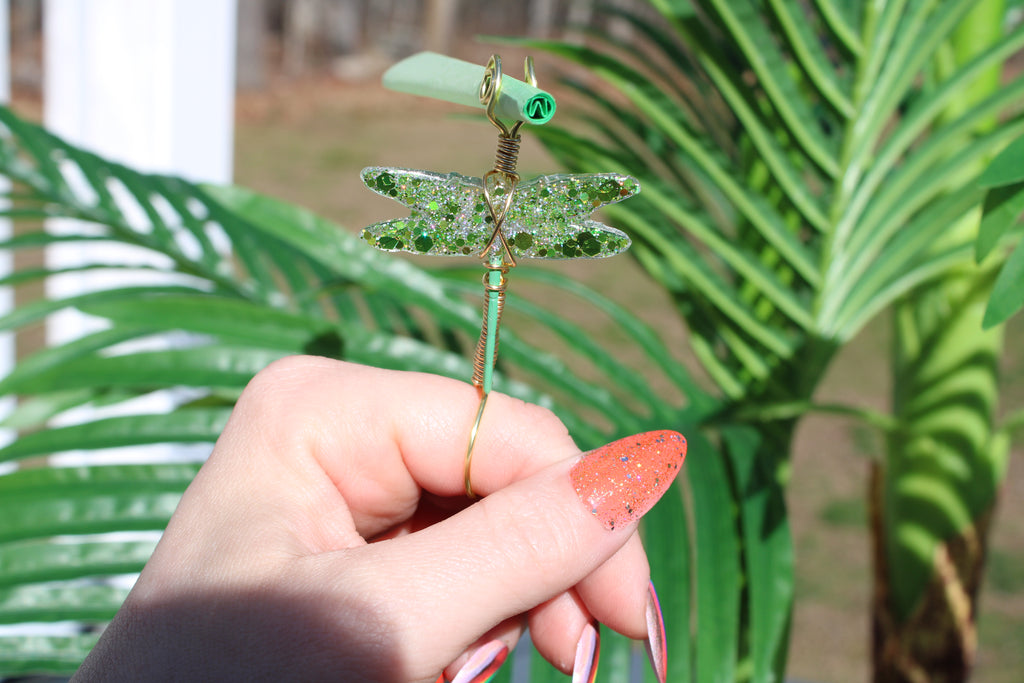 Image shows a green dragonfly smoke ring holding a green rolling paper outside 