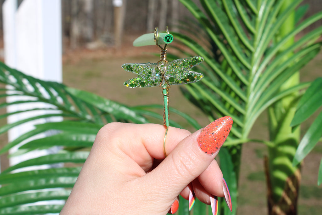 Image shows a green dragonfly smoke ring holding a green rolling paper outside 