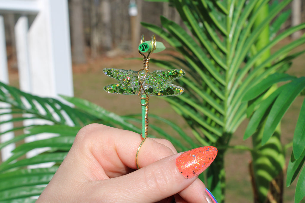 Image shows a green dragonfly smoke ring holding a green rolling paper outside 