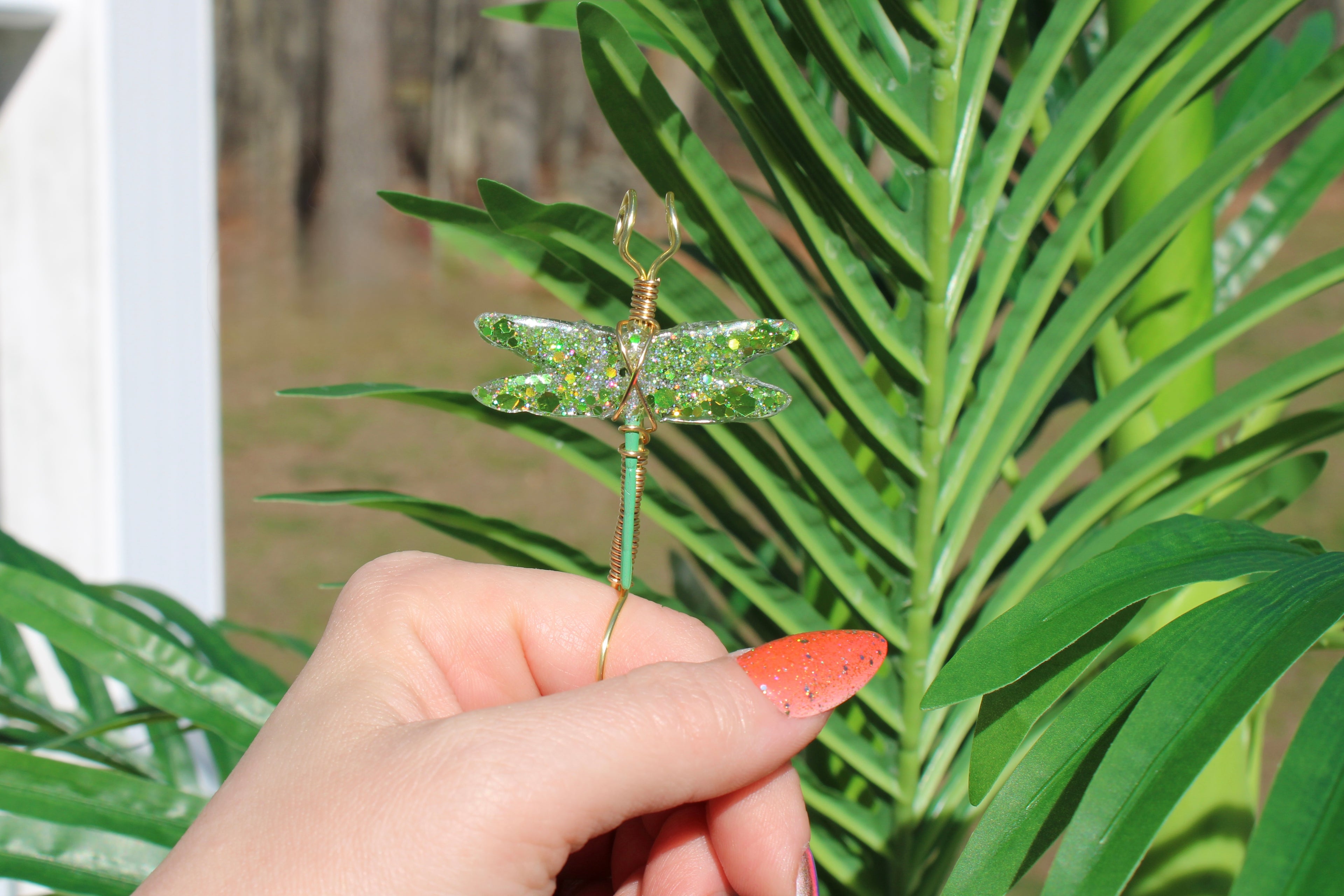 Hand holding a green decorative dragonfly smoke ring against a green leafy background
