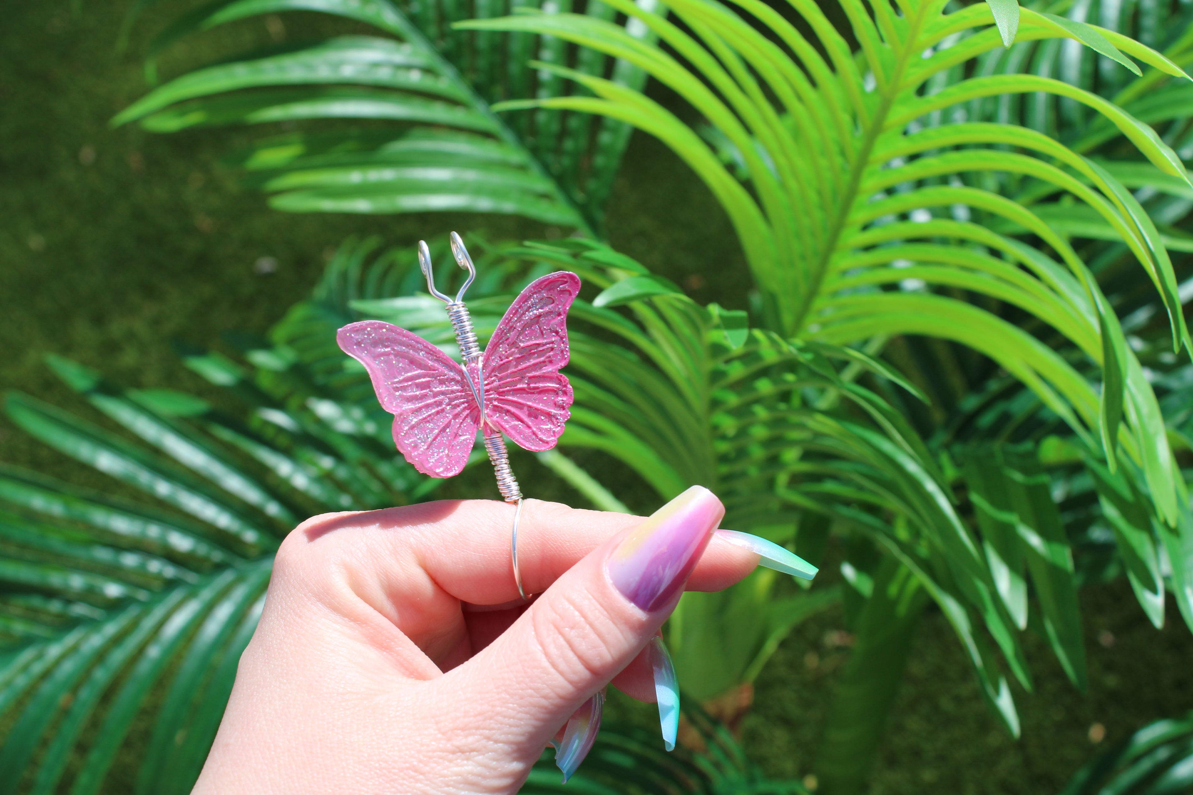 Hand holding a pink butterfly smoke ring against a green leafy background