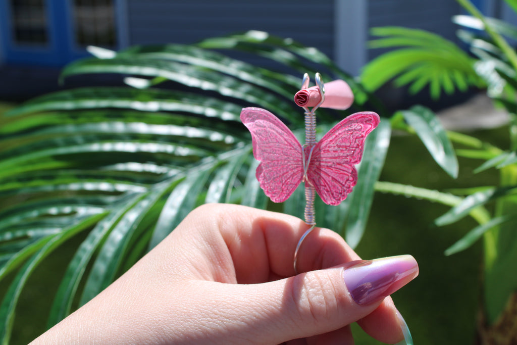 Pink butterfly smoke ring held by a hand with green foliage in the background