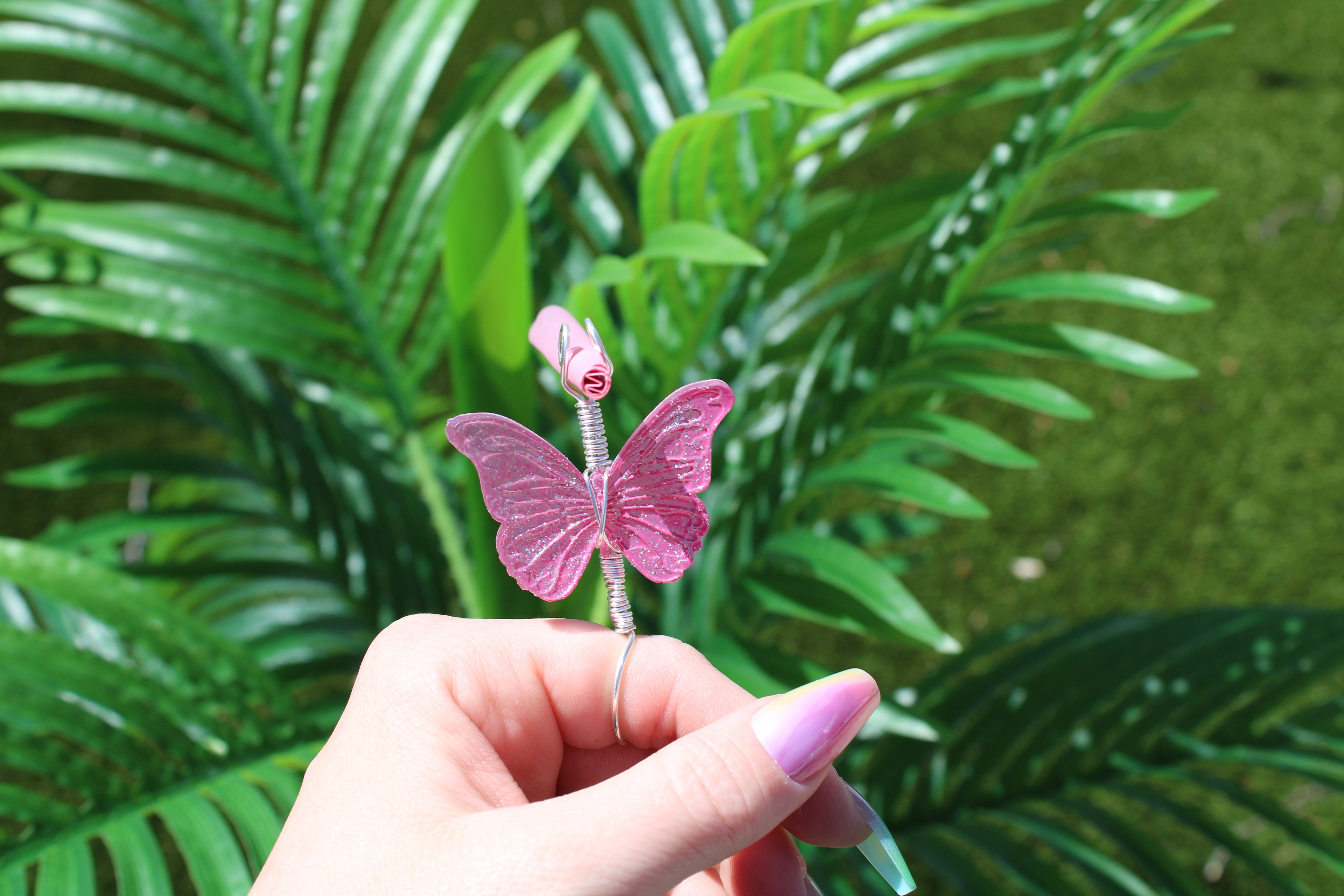 Hand holding a pink butterfly smoke ring against a green leafy background