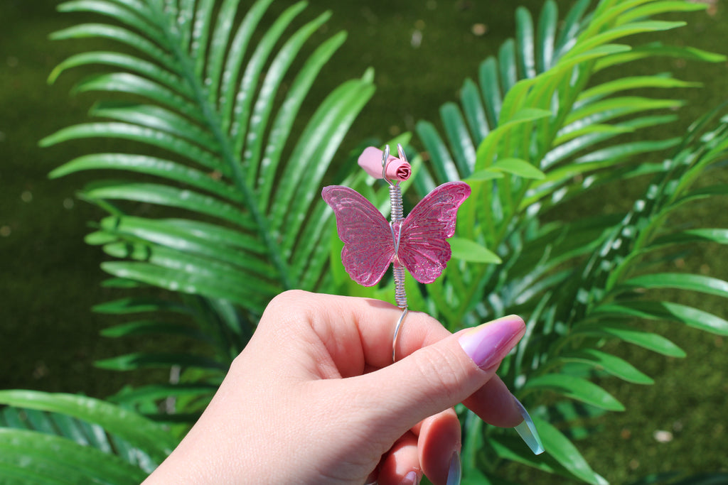 Hand holding a pink butterfly smoke ring with green leaves in the background