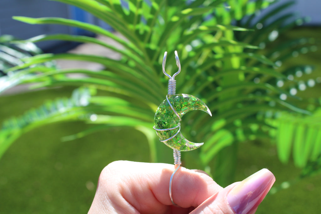 Hand holding a green moon smoke ring with wire wrapping against a blurred green plant background