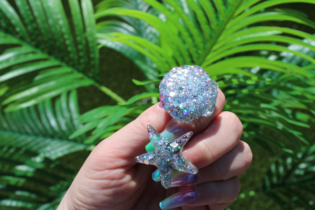 Hand holding a glittery car vent clips against a green leafy background