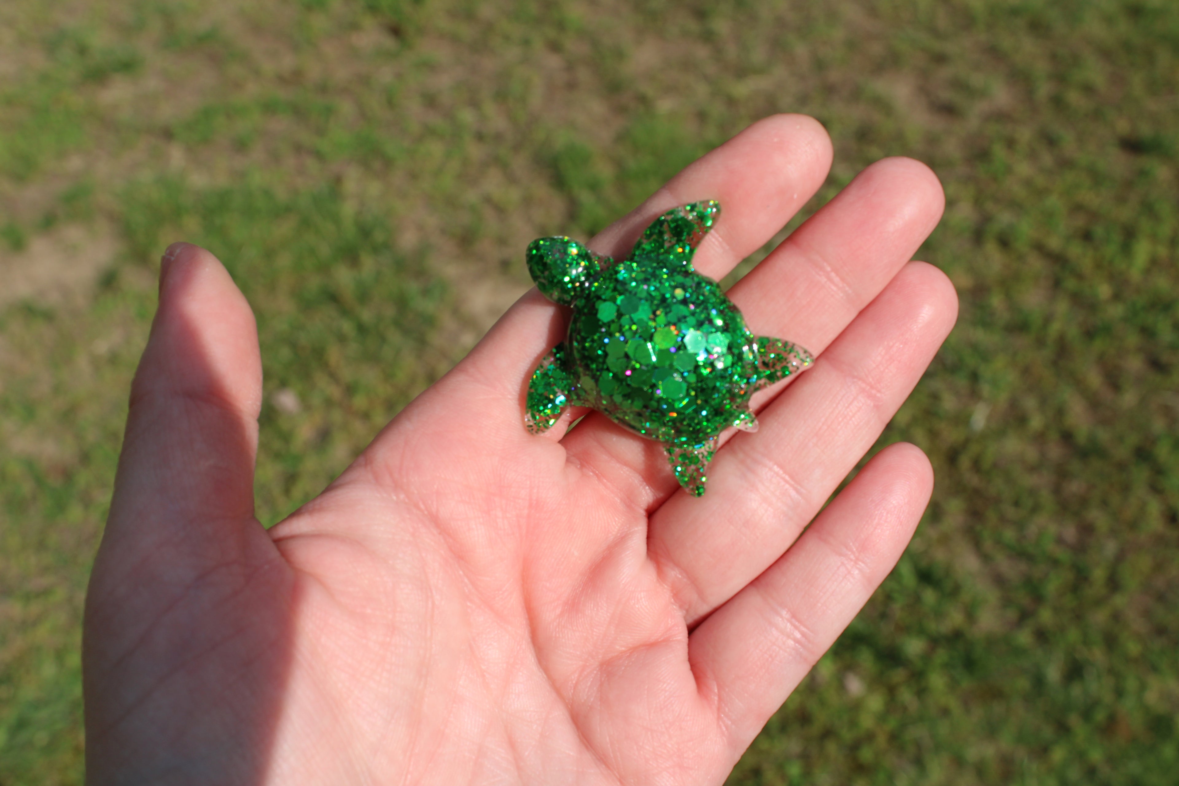 Hand holding a green glittery turtle car vent clip against a grassy background