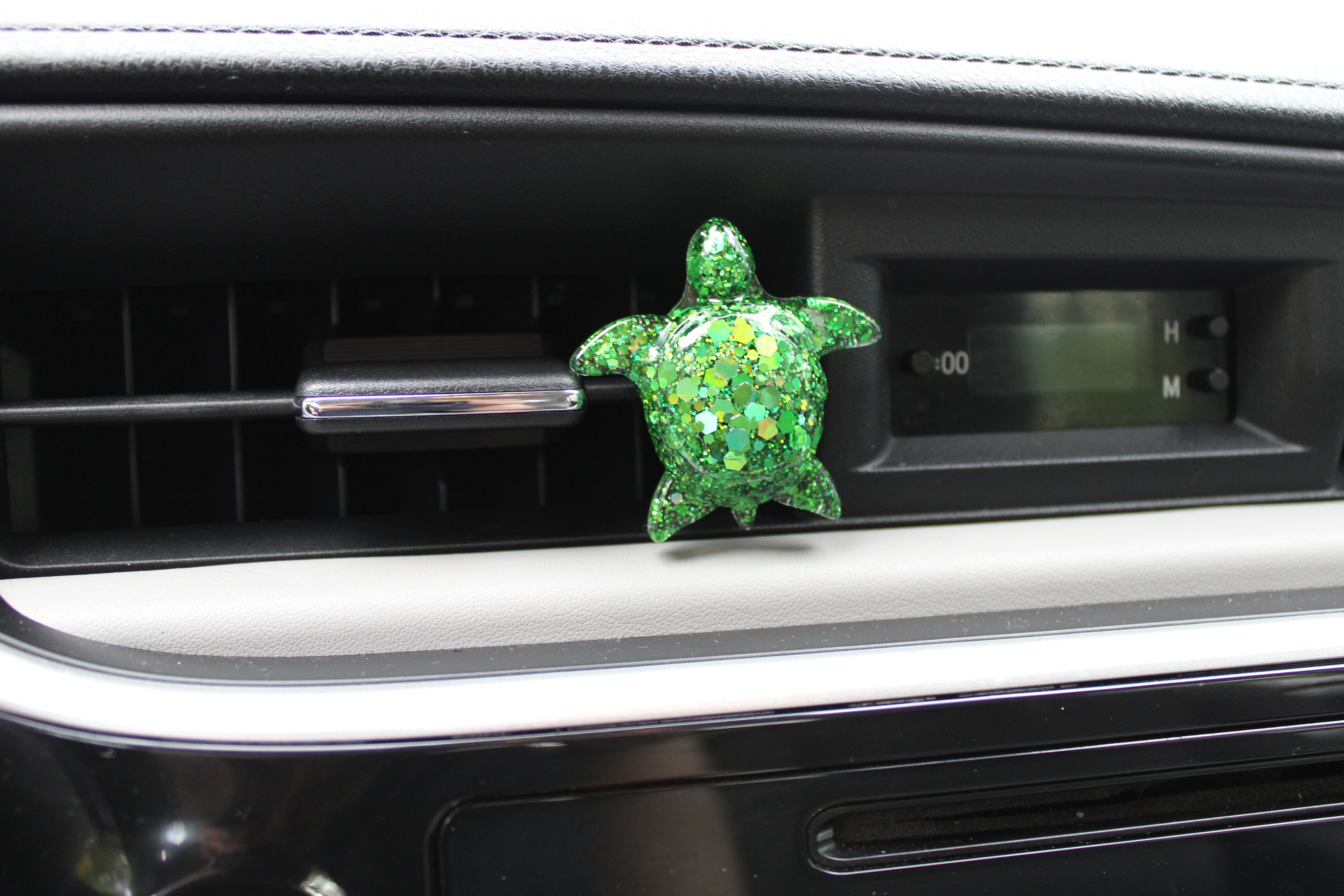 Green turtle-shaped car vent clip on a car dashboard