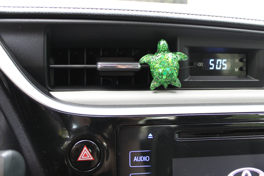 Green turtle-shaped car vent clip on a car dashboard with digital clock display.