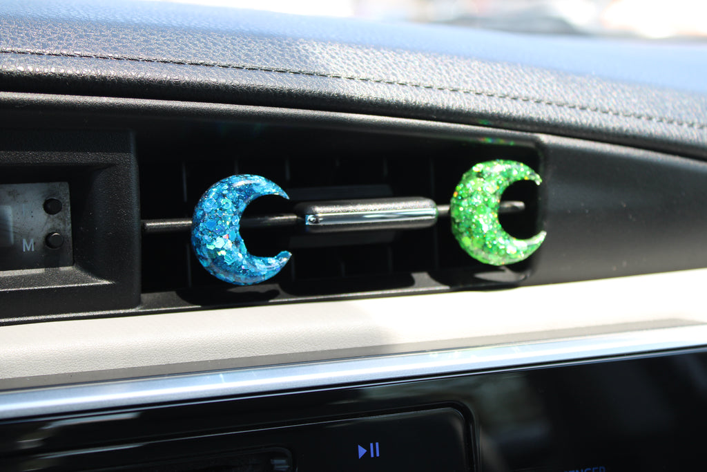 Car vent clips with blue and green crescent moon designs on a car dashboard.