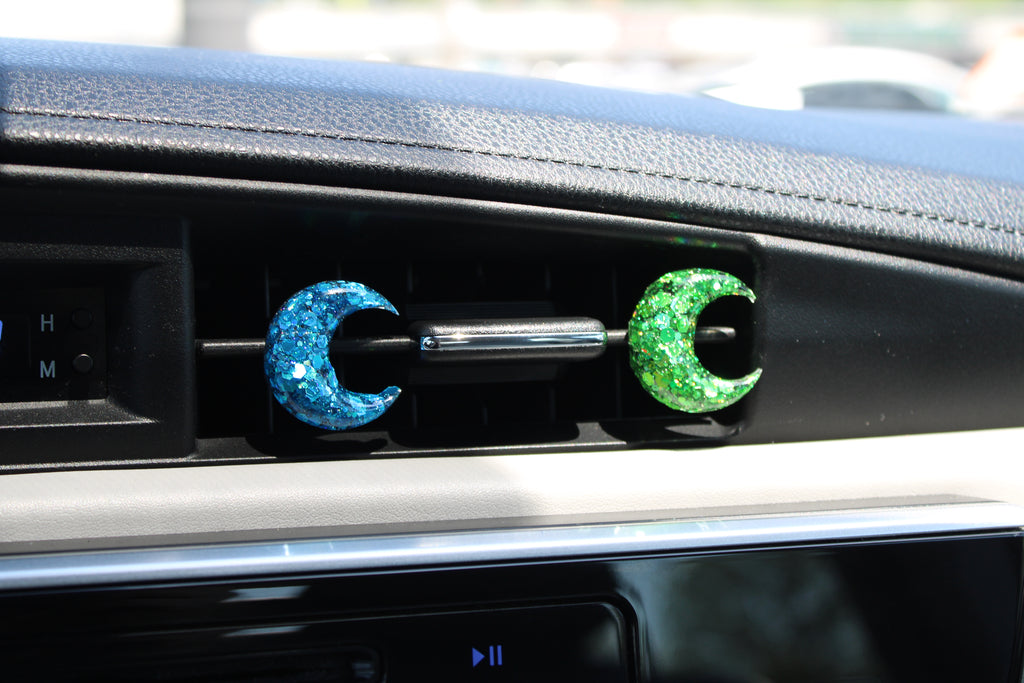 Car vent clips with blue and green crescent moon designs on a dashboard.