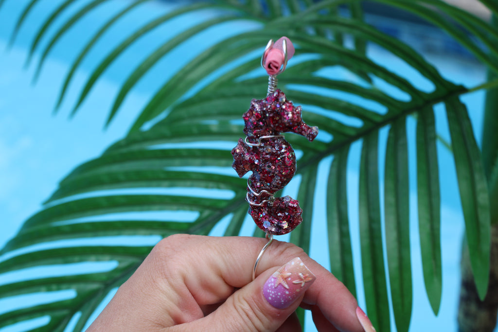 Pink seahorse-shaped smoke ring held by a hand with a palm leaf background