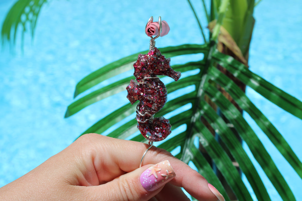 Hand holding a sparkling seahorse smoke ring with a palm leaf and blue water background