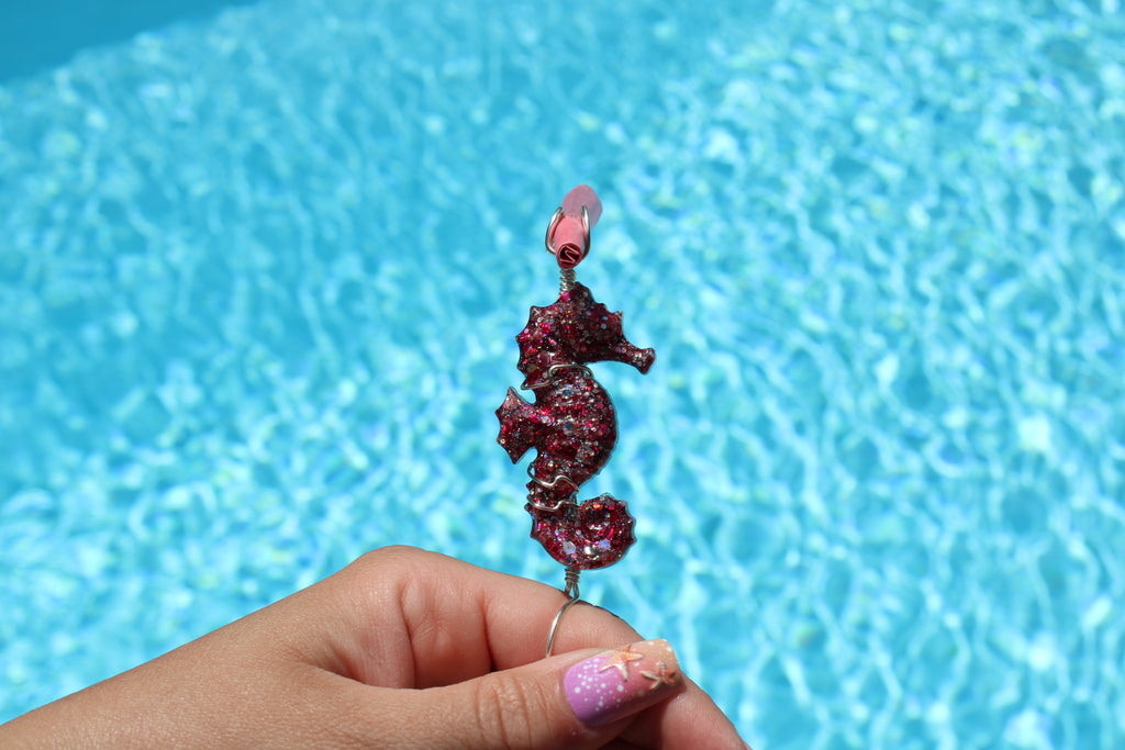 Hand holding a decorative seahorse smoke ring against a blue pool background