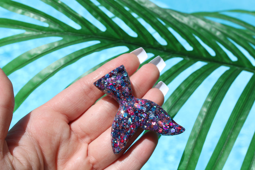 Multicolored glittery mermaid tail in a hand with palm leaves in the background