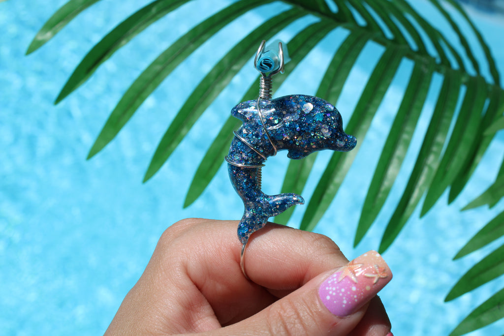 Blue glittery dolphin-shaped smoke ring held by a hand with a palm leaf background