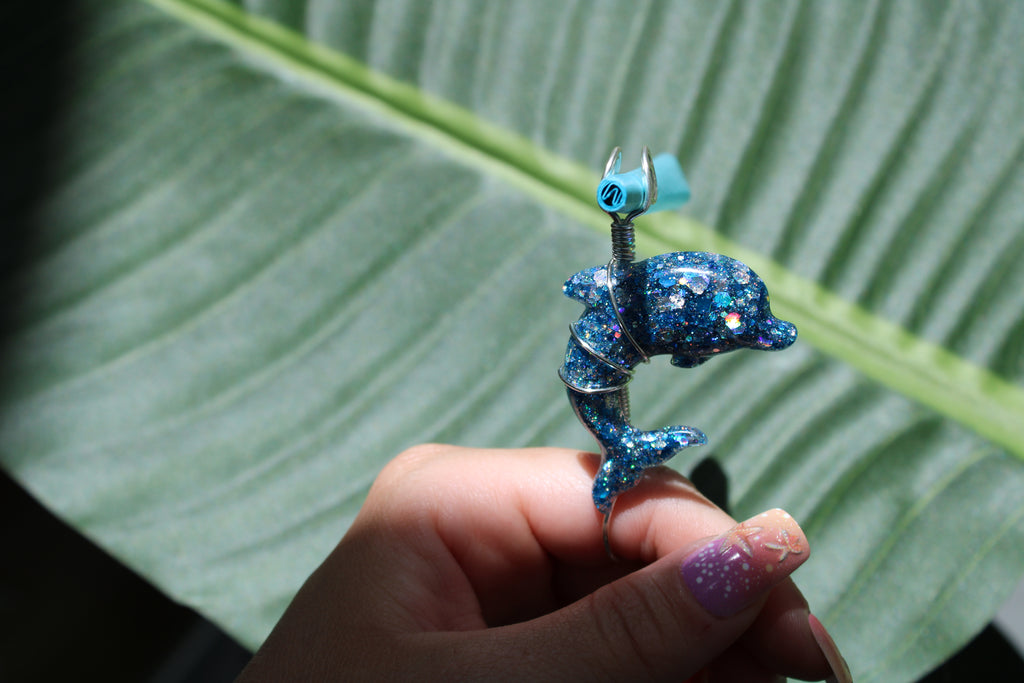Blue glittery dolphin-shaped smoke ring held against a green leaf background