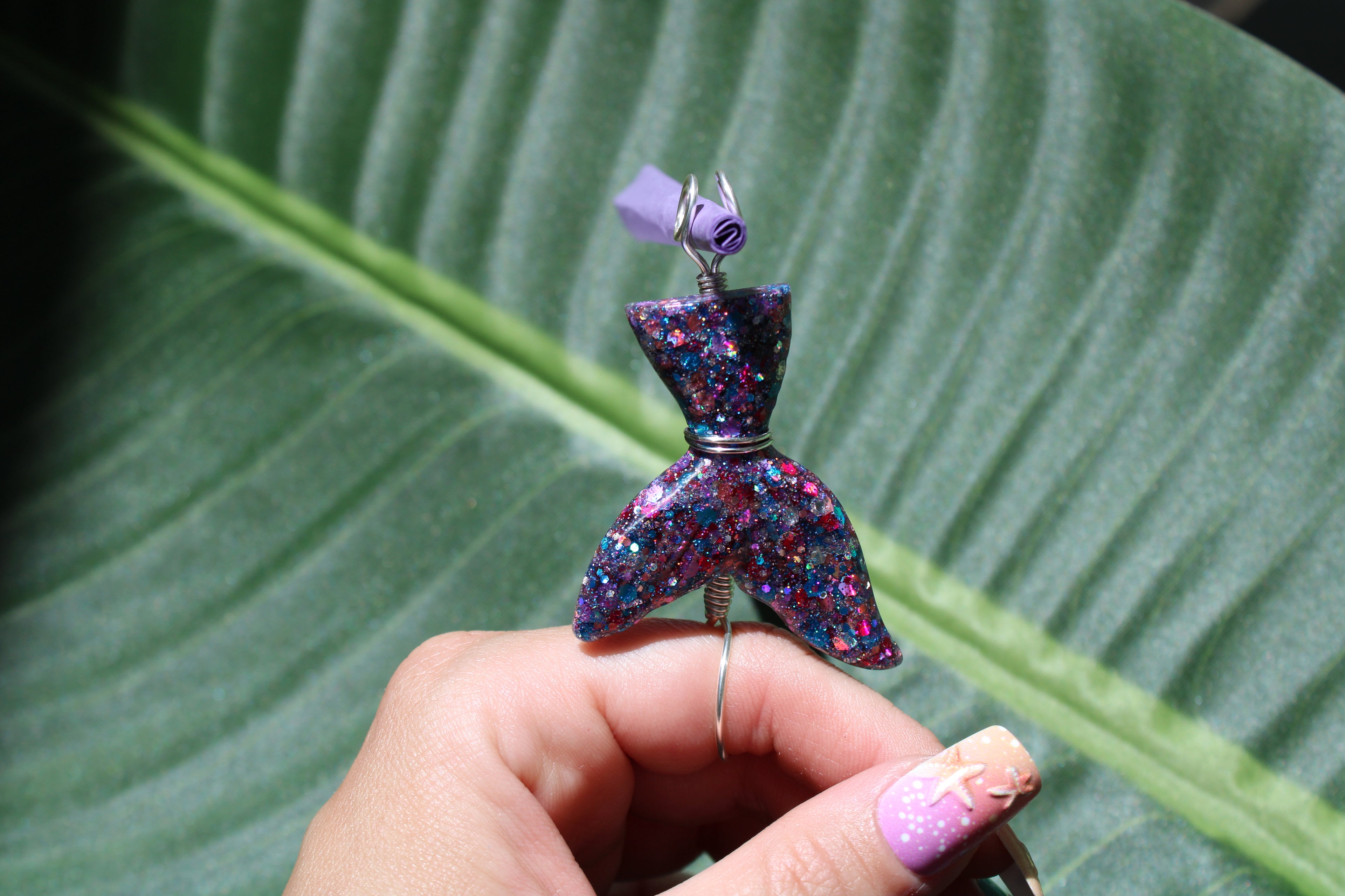 Colorful mermaid tail smoke ring held by a hand against a green leaf background