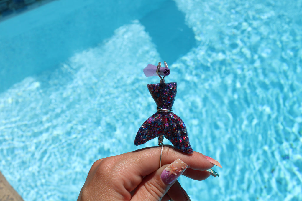 Hand holding a mermaid tail smoke ring with a pool in the background 