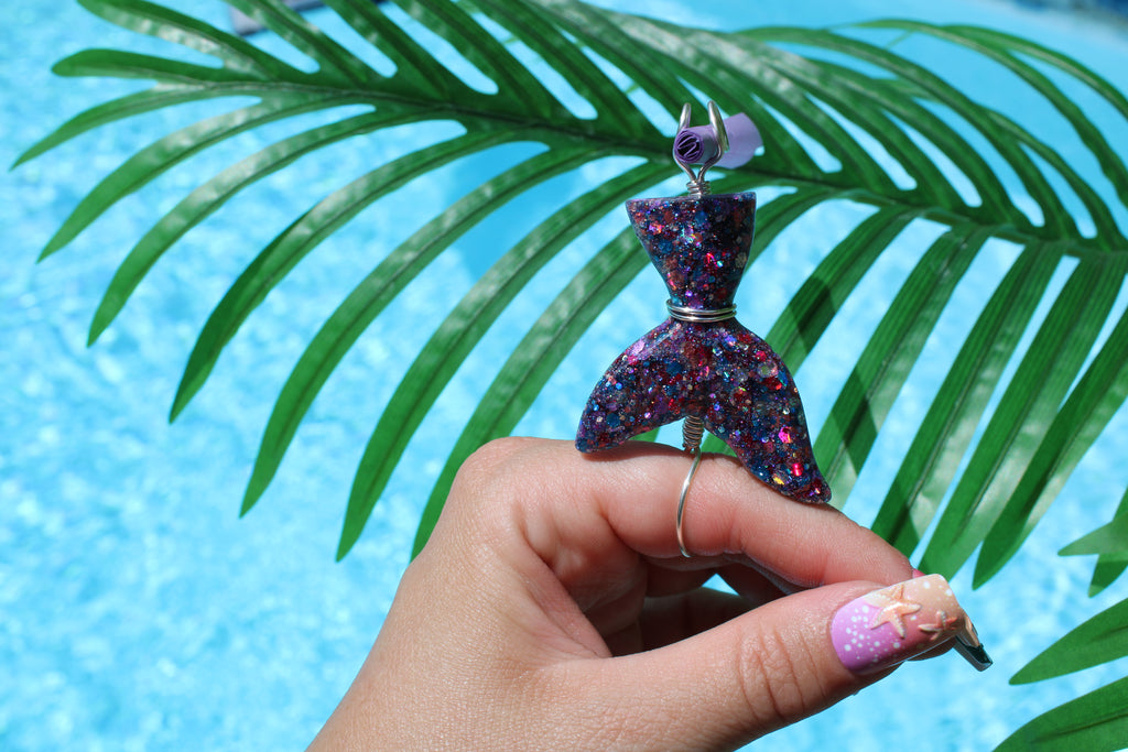 Hand holding a colorful mermaid tail smoke ring with a palm leaf and blue water background