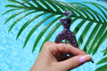 Hand holding a colorful mermaid tail smoke ring with a palm leaf and blue water background