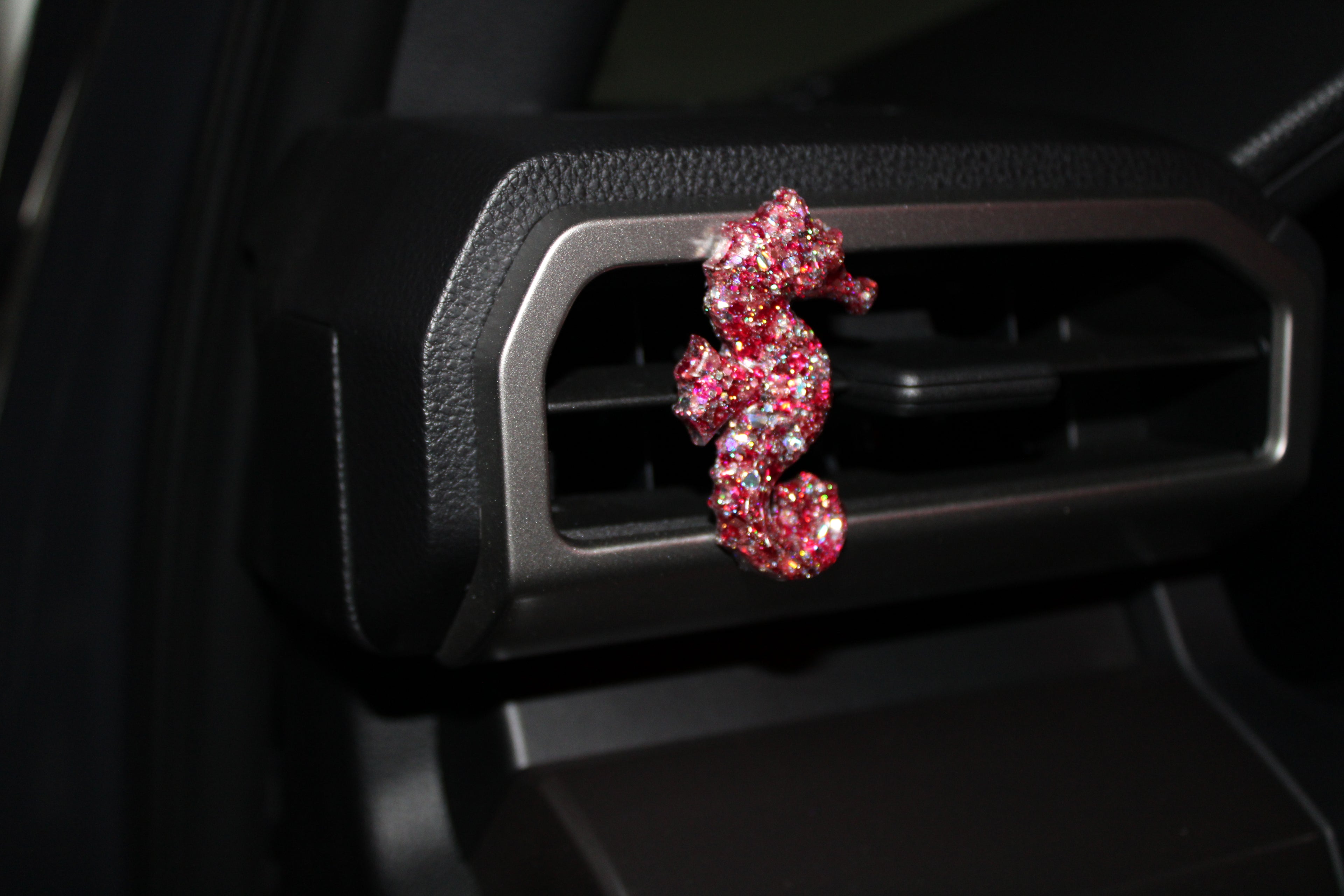 Pink seahorse-shaped car vent clip on a car's air vent.