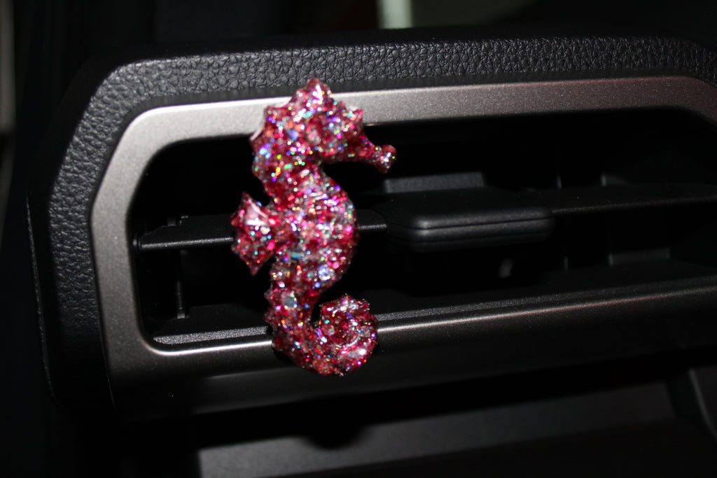 Pink glittery seahorse-shaped car vent clip on a car vent.