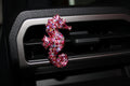 Pink glittery seahorse-shaped car vent clip on a car vent.