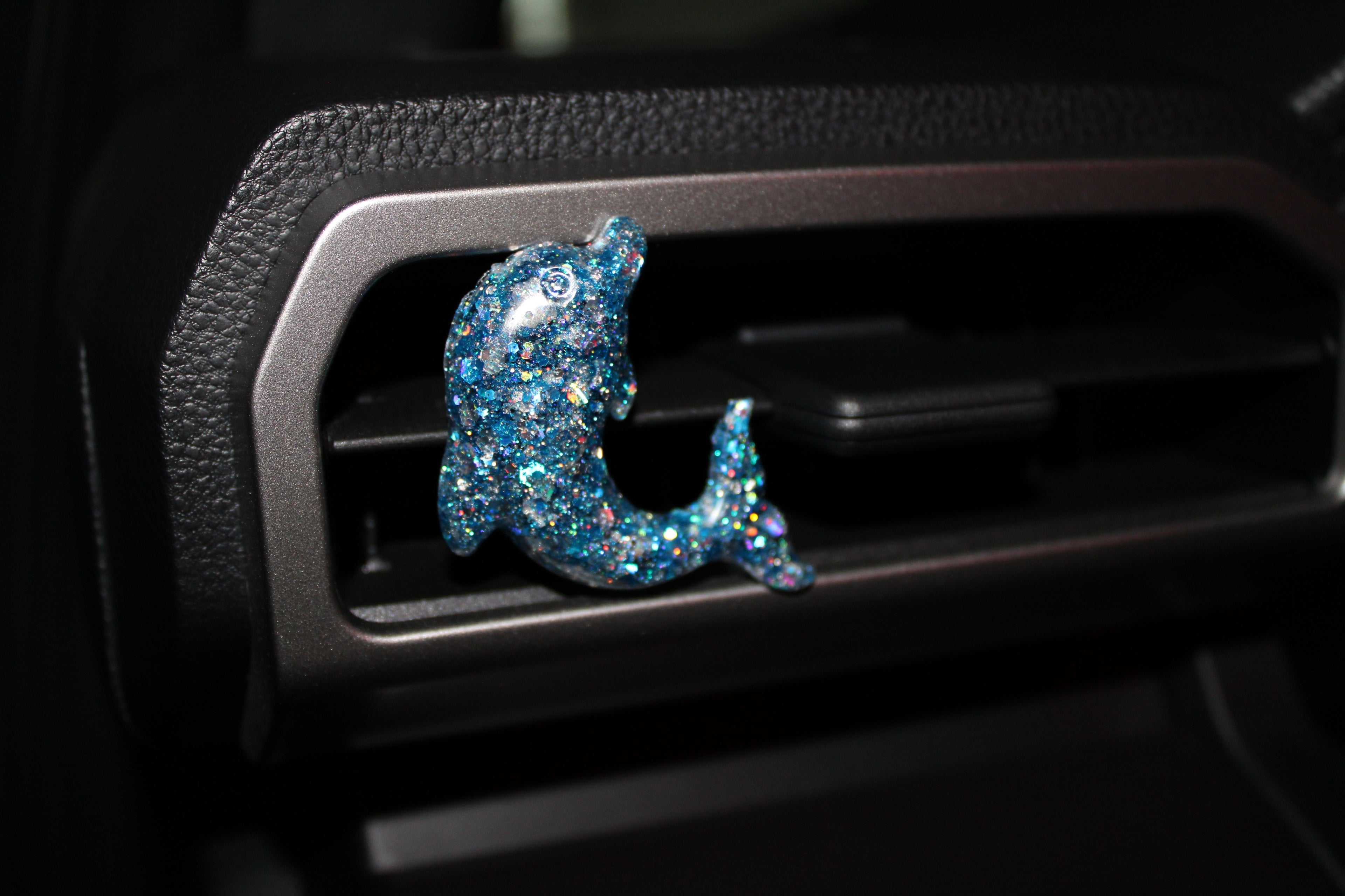 Decorative blue glittery dolphin car decor on a car vent.